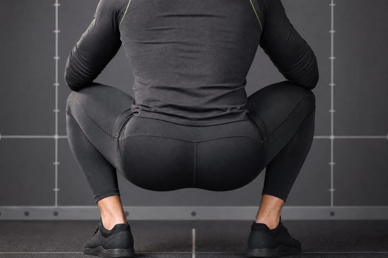 A close-fitting leg garment photographed square-on from behind at a 90 degree squat under flat, even studio lighting against a plain grey measurement backdrop