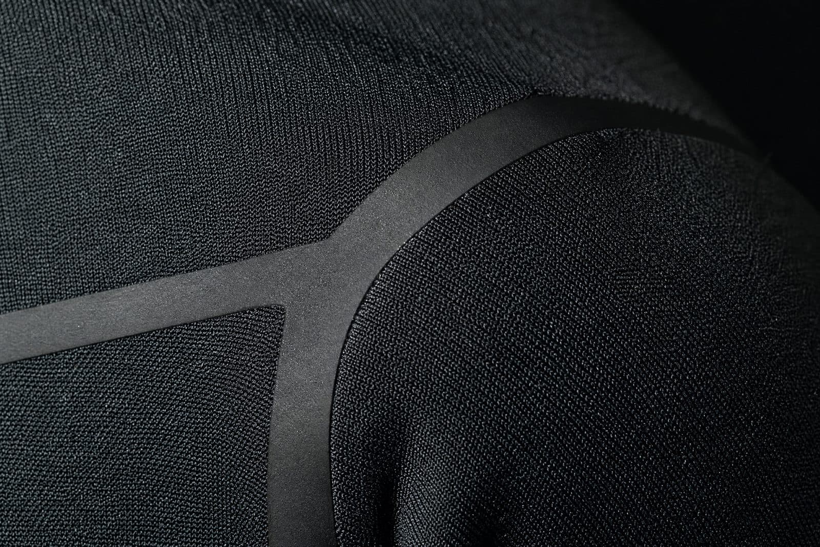 Macro photograph of a bonded seam junction on dark technical knit fabric, showing flat bonded tape running into a laser-cut edge with no stitching
